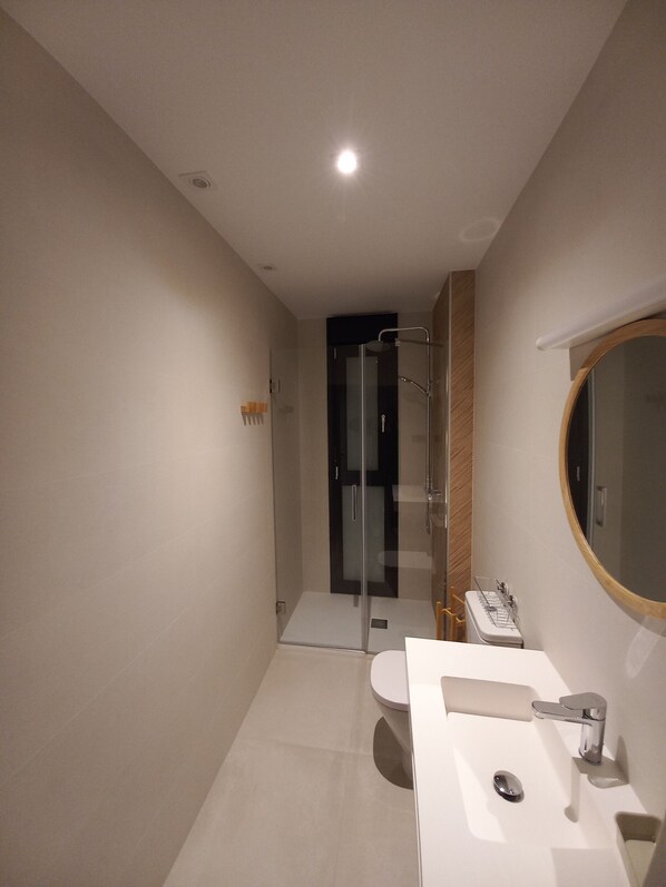 Un baño moderno con cabina de ducha de vidrio, un lavamanos blanco y un espejo redondo, y un inodoro.