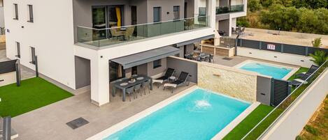 A modern villa with a rooftop terrace, a swimming pool, and a dining area.