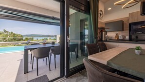 Une cuisine moderne dotée d’un four et d’un micro-ondes encastrés, un coin repas avec une table et des chaises, et une porte-fenêtre coulissante donnant sur un balcon avec vue sur la piscine.
