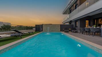 A modern outdoor pool with a stone wall, lounge chairs, and a dining area with tables and chairs.