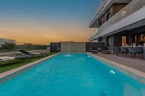 A modern outdoor pool with a stone wall, lounge chairs, and a dining area with tables and chairs.