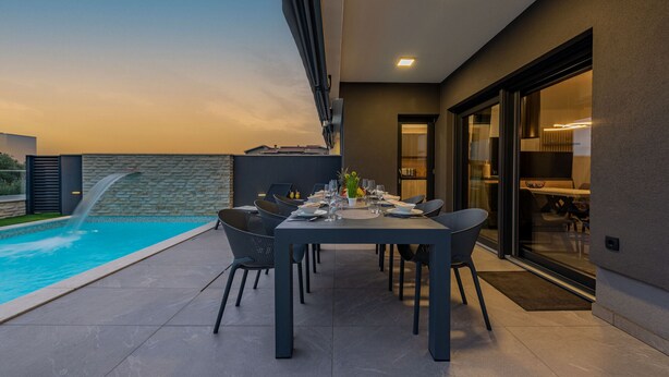 Un espace repas avec vue sur la piscine, doté de meubles modernes et d’une porte vitrée donnant sur la cuisine.