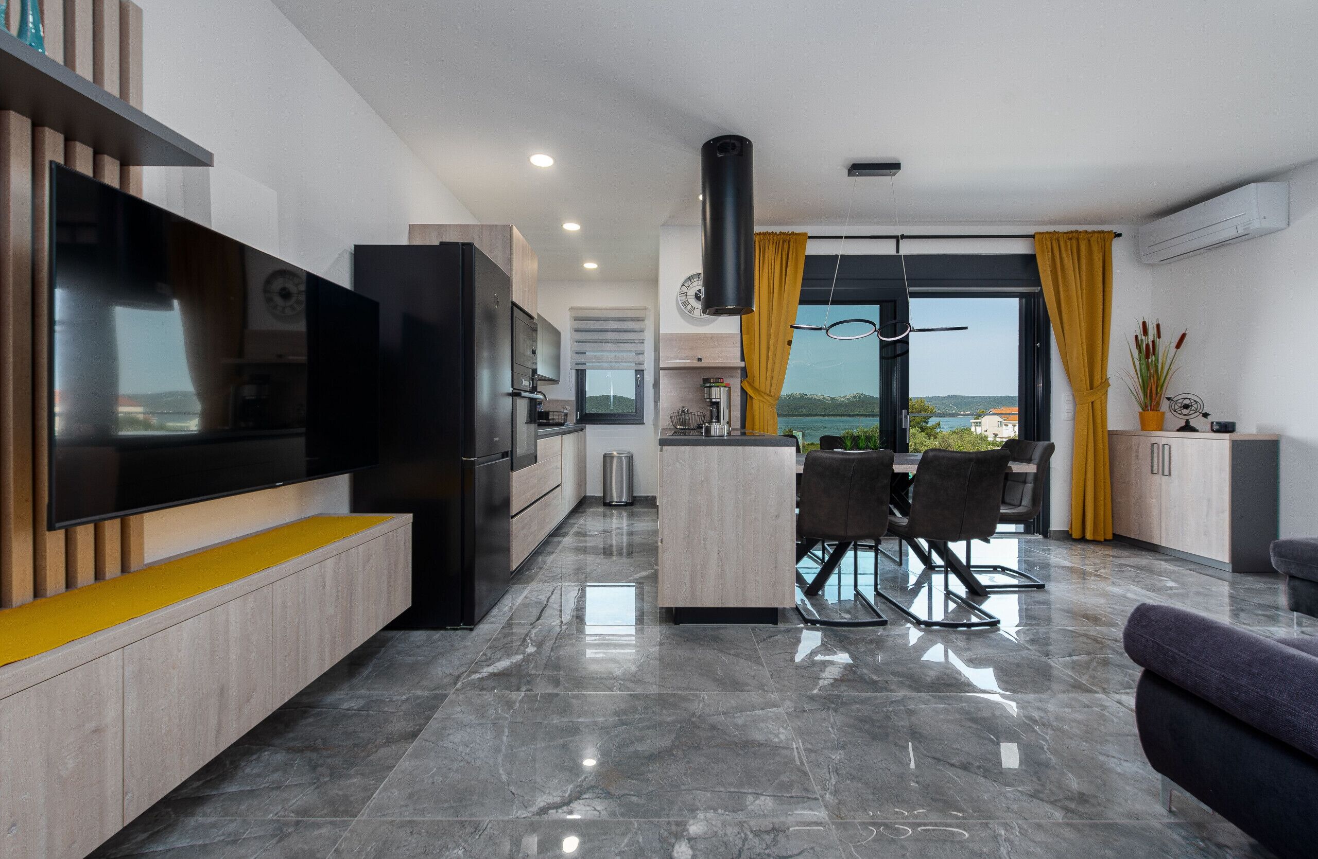 A modern kitchen with a built-in TV, a dining area with a table and chairs, and a view of the outdoors.