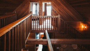 A wooden staircase leading to a lofted area with a railing, a window with curtains, and a hanging light fixture. - Endless Views: Sunsets, Sauna, Outdoor Firepit under the Stars (Max Meadows)