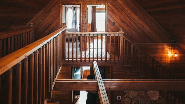 Un escalier en bois menant à une mezzanine, avec une rambarde, une fenêtre avec des rideaux et un luminaire suspendu.