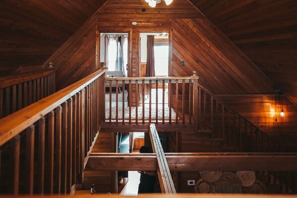 A wooden staircase leading to a lofted area with a railing, a window with curtains, and a hanging light fixture. - Stunning Long Range Views: Sunsets, Sauna, Outdoor Firepit under the Stars (Max Meadows)