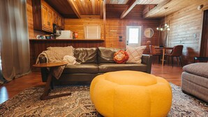 A cozy living area with a leather sofa, a yellow ottoman, and a patterned rug. - Endless Views: Sunsets, Sauna, Outdoor Firepit under the Stars (Max Meadows)