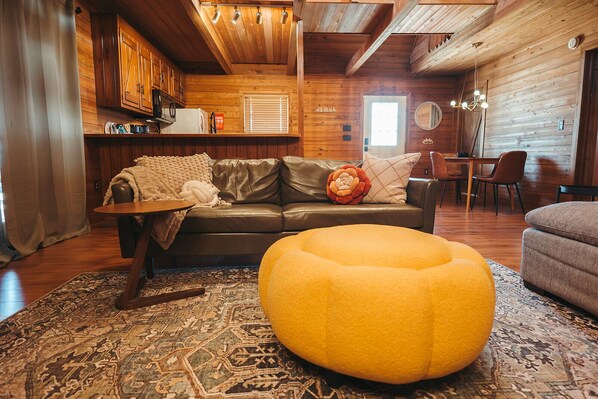 A cozy living area with a leather sofa, a yellow ottoman, and a patterned rug. - Stunning Long Range Views: Sunsets, Sauna, Outdoor Firepit under the Stars (Max Meadows)