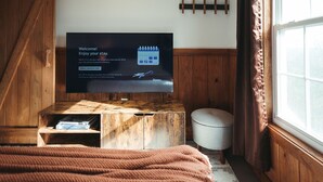 Une pièce chaleureuse avec un meuble TV en bois, un téléviseur à écran plat affichant un message de bienvenue, un petit pouf et une fenêtre avec des rideaux.