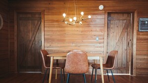 A wooden interior with a table and chairs, a hanging light fixture, and a welcome sign. - Endless Views: Sunsets, Sauna, Outdoor Firepit under the Stars (Max Meadows)