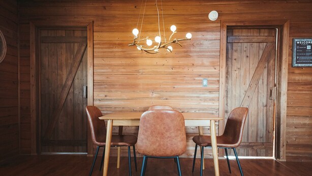 A wooden interior with a table and chairs, a hanging light fixture, and a welcome sign. - Stunning Long Range Views: Sunsets, Sauna, Outdoor Firepit under the Stars (Max Meadows)