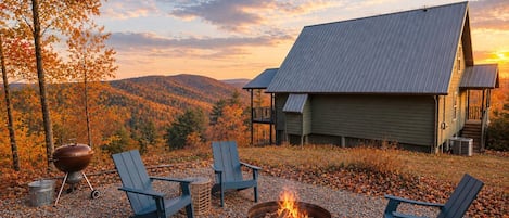 A cabin with a fireplace, outdoor seating, and a scenic view of autumn foliage and mountains.