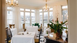 A dining area with tables set for a meal, large windows, and chandeliers. - The Lilley Mansion Bed & Breakfast (Spring Lake)