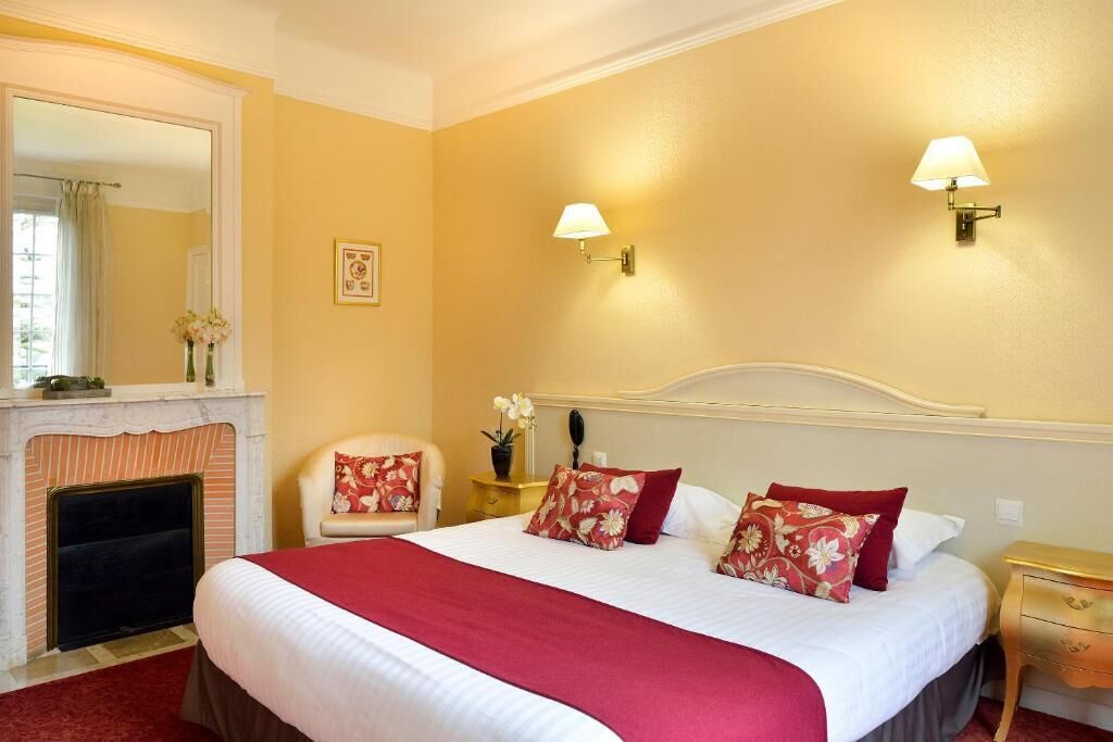 Habitación de hotel con una cama grande, chimenea, zona de estar con un sillón y dos lámparas de pared.