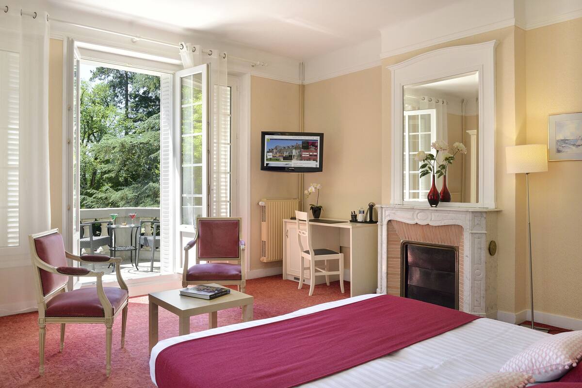 Una habitación de hotel con cama, escritorio, dos sillas, chimenea y televisión.