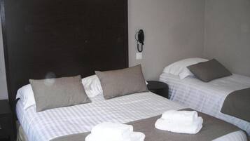 A hotel room with two beds, each with a pillow and a blanket. There is a phone on the wall and towels on the beds.