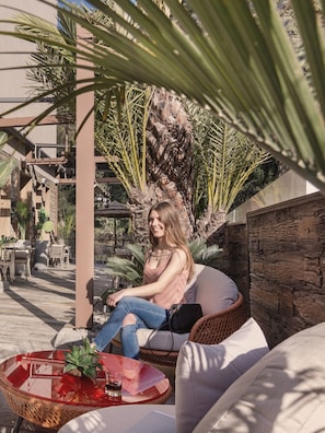 A woman seated on a wicker chair in an outdoor patio area with a glass table, surrounded by plants and a stone wall. - Casa Coco Boutique Hotel Spa Adults Only (Lloret de Mar)