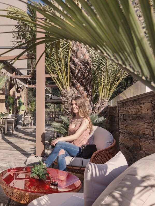 A woman seated on a wicker chair in an outdoor patio area with a glass table, surrounded by plants and a stone wall. - Casa Coco Boutique Hotel Spa Adults Only (Lloret de Mar)