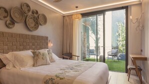 Ein modernes Schlafzimmer mit einem großen Bett, einem Deckenventilator, Blick auf den Garten durch eine Schiebetür und Wandkunst aus gewebten Materialien.