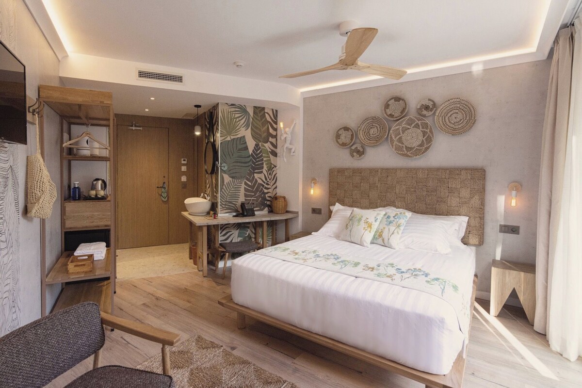 Un dormitorio moderno con una cama grande, un escritorio de madera, un ventilador de techo y una pared decorada con arte de pared tejido.