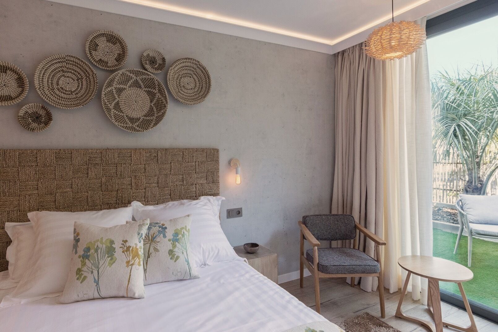 A bedroom with a large bed, a chair, a small table, and a view of the outdoors.