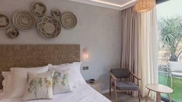 A bedroom with a large bed, a chair, a small table, and a view of the outdoors.