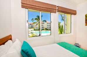 Ein Hotelzimmer mit einem Bett, einem Fenster mit Blick auf einen Pool und Palmen sowie einem Fensterrollo.