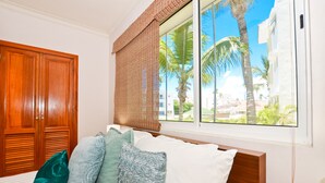 Une chambre d’hôtel avec un lit, une fenêtre donnant sur des palmiers et une armoire en bois.