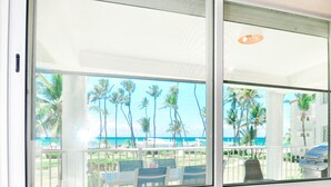 Une chambre avec vue sur une plage et des palmiers, visible par une fenêtre.