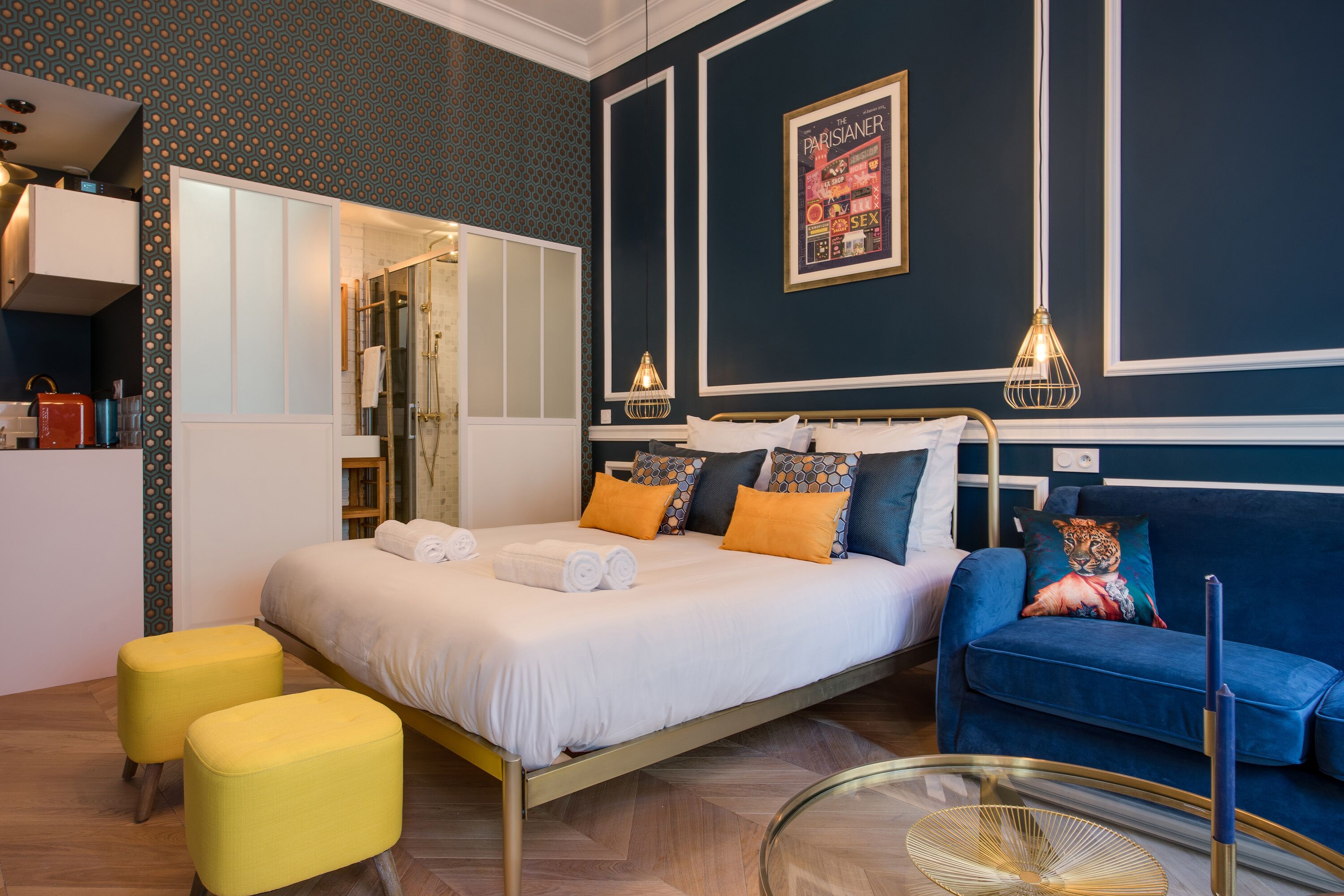 A modern hotel room with a bed, a blue sofa, a glass coffee table, and a shower area.
