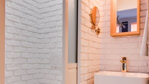 A bathroom with a white brick wall, a white toilet, a wooden vanity with a mirror, and patterned floor tiles. - The Blue Elysée (Paris)