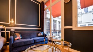 A modern living room with a blue sofa, a glass coffee table, and a view of the city through large windows. - The Blue Elysée (Paris)