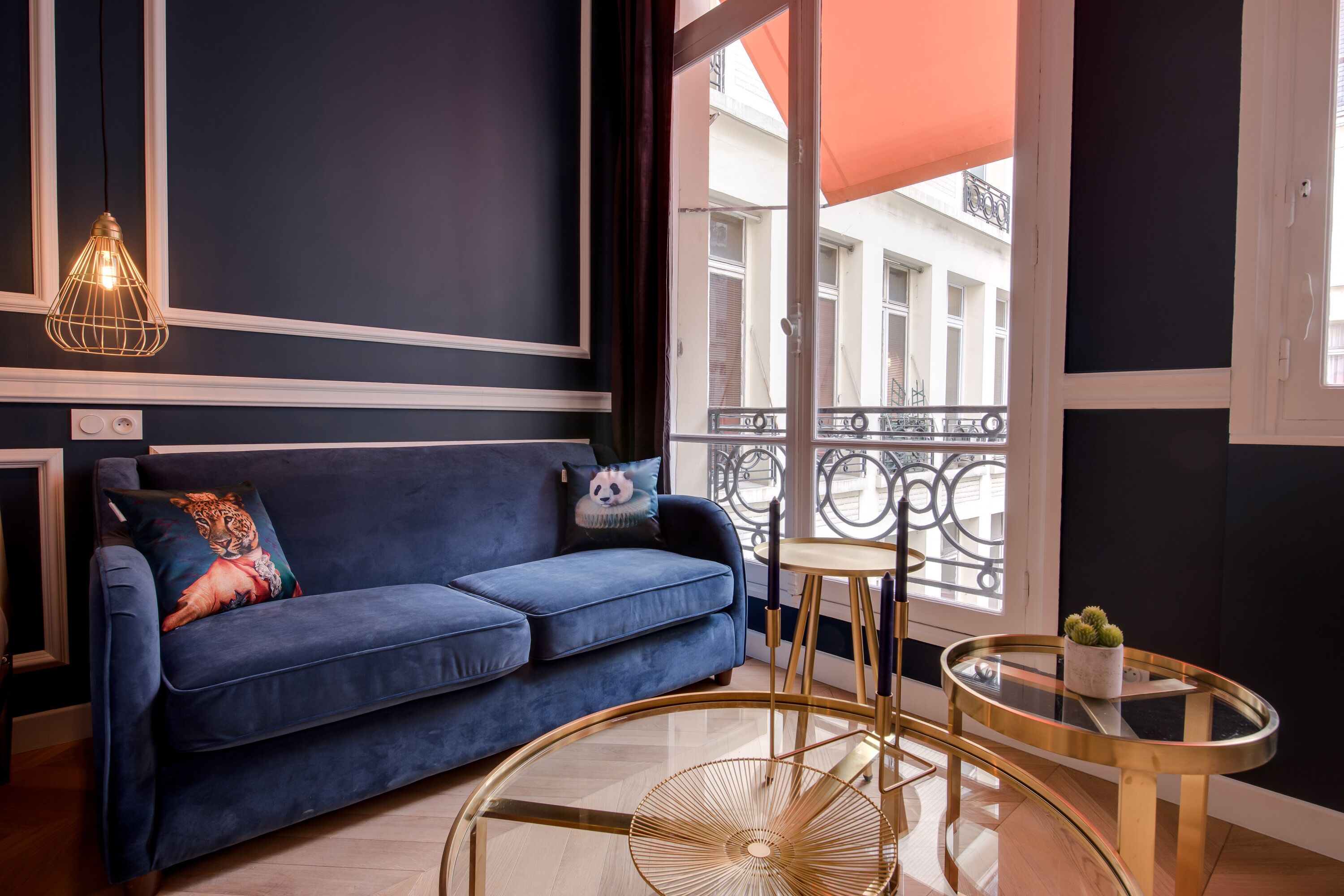 A modern living room with a blue sofa, a round gold table, and a hanging light fixture.