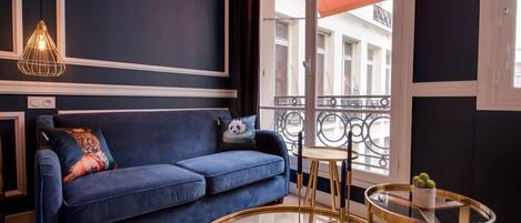 A modern living room with a blue sofa, a round gold table, and a hanging light fixture.