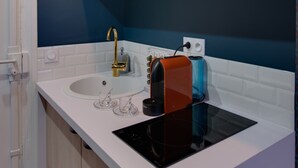 A modern kitchen with a white countertop, a black induction cooktop, a gold faucet, and three pendant lights. - The Blue Elysée (Paris)