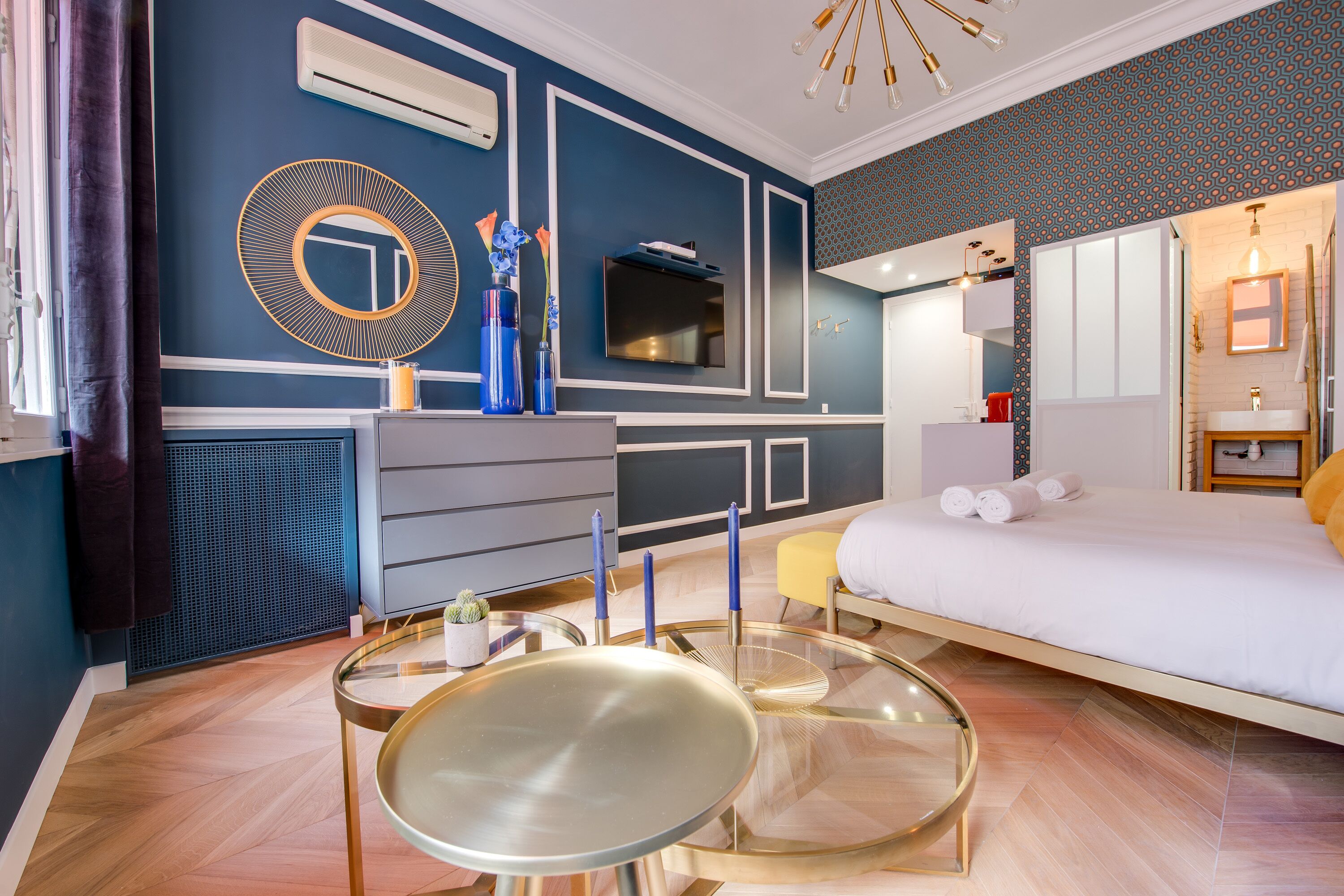 Un dormitorio moderno con una cama, un televisor, un aparador y una mesa redonda de vidrio.