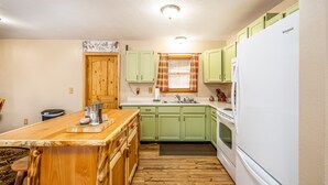 A kitchen with green cabinets, a wooden island, a white refrigerator, and a window with plaid curtains. -  Arrowhead Sanctuary!! Beautiful Cabin! Deck with Fire Pit & Incredible Views! (Cimarron)