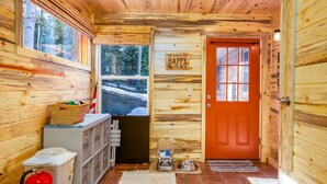 A cabin interior with wooden walls, a red door, a window with a view of a snowy landscape, a basket, a water dispenser, and a fire extinguisher. -  Arrowhead Sanctuary!! Beautiful Cabin! Deck with Fire Pit & Incredible Views! (Cimarron)