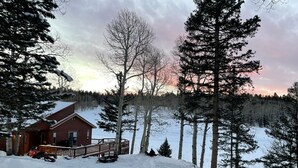 A log cabin with a deck, surrounded by snow-covered ground and trees. -  Arrowhead Sanctuary!! Beautiful Cabin! Deck with Fire Pit & Incredible Views! (Cimarron)