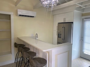 Una cocina con encimera blanca, un refrigerador de acero inoxidable y una zona con taburetes de bar.