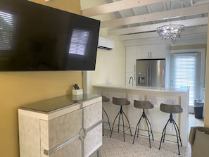 Una cocina moderna con un televisor grande, taburetes de bar y un refrigerador.