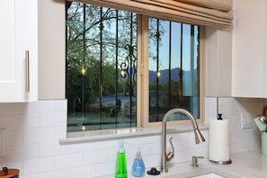 A kitchen with a window, white cabinets, a stainless steel faucet, and a roll of paper towels. - Tierra Velo - HGTV Style in East Tucson (Tucson)