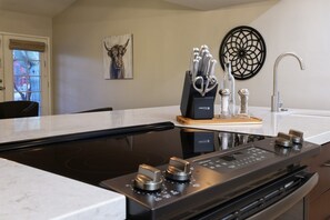 A kitchen with a black induction cooktop, a wooden cutting board with utensils, a decorative wall piece, and a modern faucet. - Tierra Velo - HGTV Style in East Tucson (Tucson)