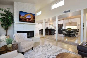 A spacious living room with a fireplace, a dining area with a large table, and a kitchen in the background.