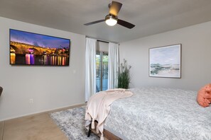 A bedroom with a bed, a ceiling fan, a TV, and a window with curtains. - Tierra Velo - HGTV Style in East Tucson (Tucson)
