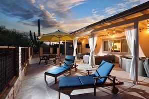 A covered outdoor patio with lounge chairs, a table, and an umbrella. - Tierra Velo - HGTV Style in East Tucson (Tucson)