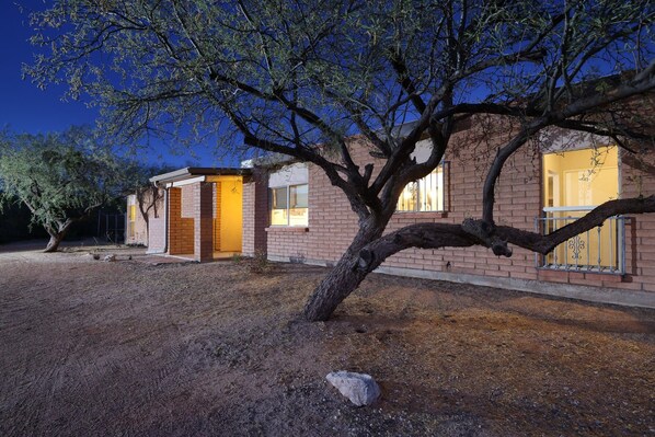 A two-story house with a brick exterior, a large tree in front, and a well-lit entrance. - Tierra Velo - HGTV Style in East Tucson (Tucson)