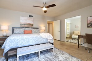A bedroom with a bed, bedside lamps, a ceiling fan, a bench, a desk, and a chair. - Tierra Velo - HGTV Style in East Tucson (Tucson)