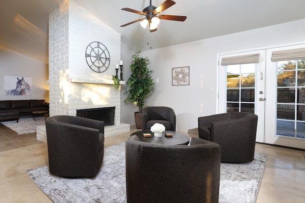 A living room with a fireplace, three dark armchairs, a coffee table, and a ceiling fan. - Tierra Velo - HGTV Style in East Tucson (Tucson)