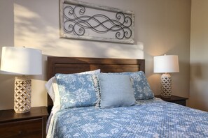 A neatly made bed with a floral-patterned bedspread, two bedside lamps with decorative bases, and a wall-mounted decorative piece above the bed. - Tierra Velo - HGTV Style in East Tucson (Tucson)